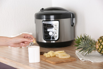 Woman putting pineapple into container with delicious fresh yogurt made in modern multi cooker on table, closeup