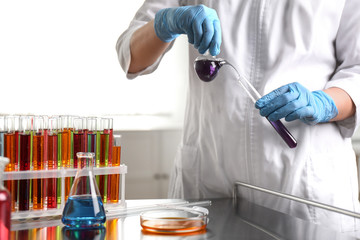 Scientist pouring liquid from retort flask into test tube at laboratory. Solution chemistry