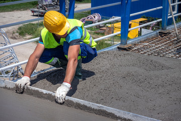 Worker with yellow helmet straighten and smoothing fresh concrete on a construction site