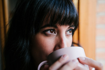 young caucasian woman at home by the window having a cup of coffee or tea. Morning and relax concept. Lifestyle indoors
