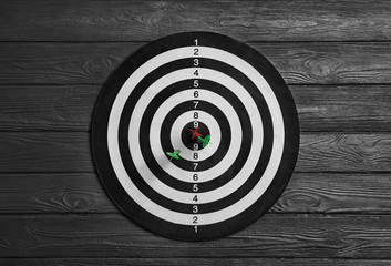 Dart board with color arrows on black wooden background, top view