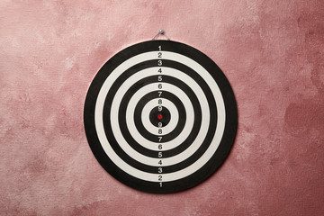 Dart board hanging on pink textured wall