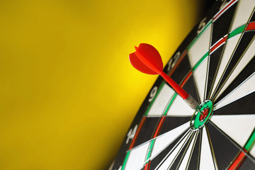Red arrow hitting target on dart board against yellow background. Space for text