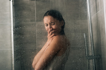 beautiful sad woman covering face and crying in shower at home