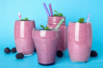 Glasses and mason jar with tasty blackberry smoothie on blue background