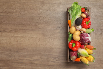 Crate with different fresh vegetables on wooden background, top view. Space for text