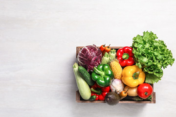 Crate with different fresh vegetables on light background, top view. Space for text