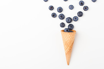 Ice cream cone filled with .blueberries on a white background. Berries fall out from a waffle cone.