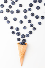 Ice cream cone filled with .blueberries on a white background. Berries fall out from a waffle cone.
