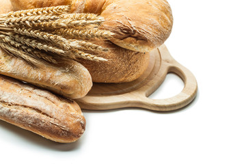 loafs of bread and wheat ears on carving board isolated