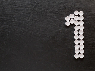 Fototapeta na wymiar Number one sign made of pills on a black textured background, Copy space.