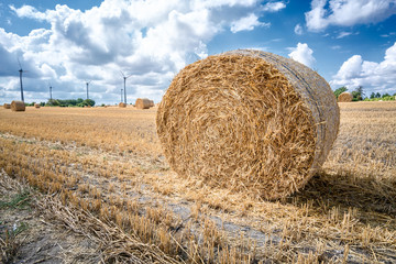 Big straw bale on field in summer-horizontal..Wind farms in background.