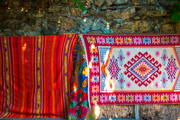 Carpets embroidered from threads of various bright colors. Carpets are hung on a stone wall in a...