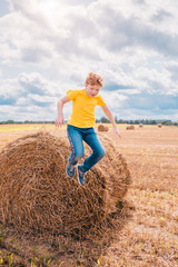 Naklejka na ściany i meble Red-haired Caucasian boy indulges on a farm field jumping from a haystack