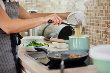 Obraz na płótnie Canvas Caucasian woman in apron standing next to stove and preparing spaghetti. Preparation of italian food concept.