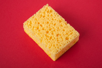 Single yellow sponge on red colored paper background, copy space