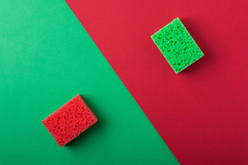 Two green and red sponges on green and red colored paper background, copy space, top view, flat lay