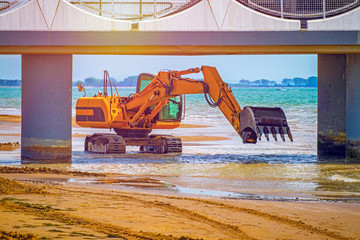 orange crawler tractor with bucket, construction work on sandy beach