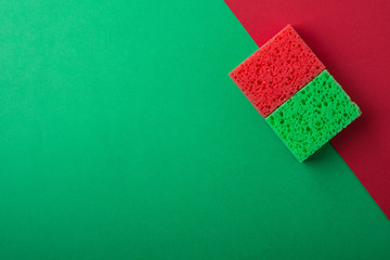 Two green and red sponges on green and red colored paper background, copy space, top view, flat lay
