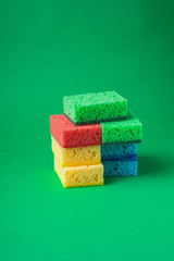Stack of sponges in red, blue, green, yellow colors on green paper background, close up