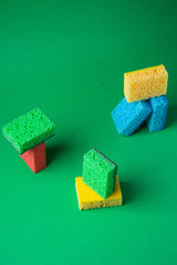 Stack geometric blocks construction abstract sponges in red, yellow, blue, green colors, on green paper background, copy space
