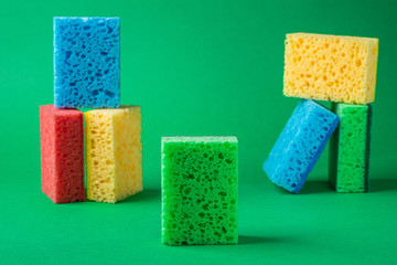 Stack geometric blocks construction abstract sponges in red, yellow, blue, green colors, on green paper background, copy space