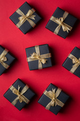 Black gift box with golden ribbons on red paper background, pattern, texture, isolated, top view, flat lay