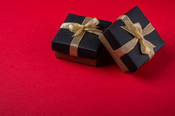 Two black gift box with golden ribbons on red paper background, isolated, copy space