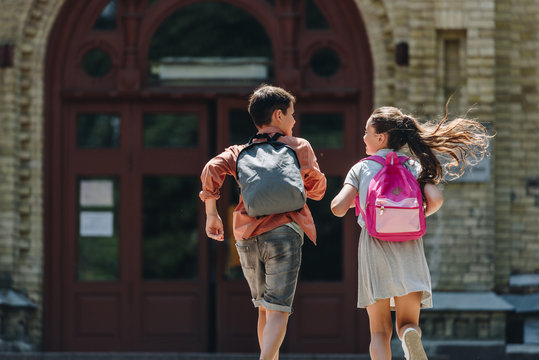 back view of two schoolkids with backpacks running in schoolyard
