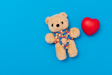 World Autism Awareness day, mental health care concept. Teddy bear with red heart and ribbon puzzle pattern. On blue background