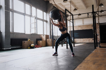 Woman doing exercise with heavy medicine ball in gym.