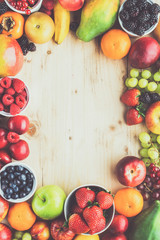 Rainbow fruits background circle frame, strawberries raspberries oranges plums apples kiwis grapes blueberries mango persimmon on light wooden table, top view, copy space, toned, selective focus
