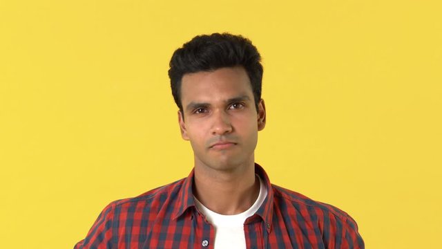Portrait of handsome serious young Indian man in plaid shirt saying yes by shaking his head against yellow background