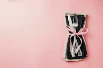 Black setting: plates, inen napkin and silverware on pink background. Top view.