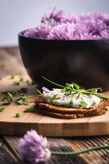 A delicious garlic and chive cream cheese spread on herbed crackers next to a bowl of purple chive flowers.