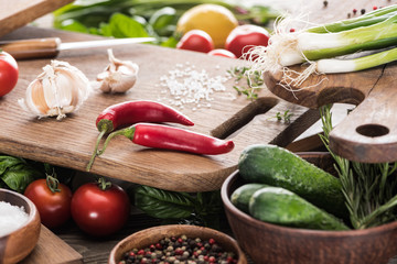 selective focus of cutting boards, cherry tomatoes, salt, garlics, cucumbers, knife, greenery, lemon, chili peppers and spices