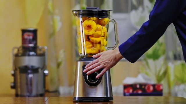 Woman making peach smoothie in blender jar. Preparing fresh vegan drink with juice machine in home kitchen. Healthy eating lifestyle, detox diet. Mixing fruit in a food processor. Slow motion.