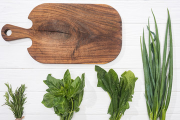 top view of wooden cutting board and greenery on white table