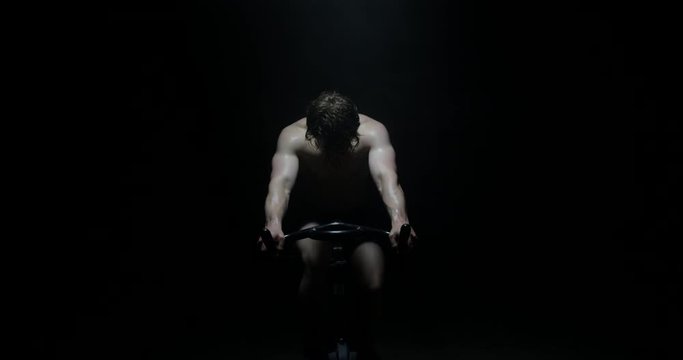 Portrait Of Handsome Man On Exercise Bike Training Exercising As Smoke Falls On Him In A Dark Background
