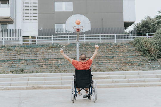 man in a wheelchair plays basketball alone in a city park