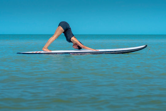Woman on paddleboard doing yoga at sea, down dog position, parvatasana