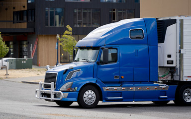 Bright blue bonnet big rig semi truck unloaded commercial cargo from refrigerator semi trailer on...