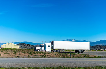 Fototapeta na wymiar Classic big rig semi truck transporting cargo in refrigerated semi trailer driving on the road in Utah