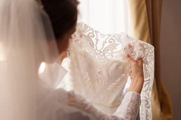 Bride holding white wedding dress with lace, embroidery. Bride getting ready