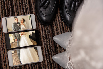 Creative wedding photo. Portrait of bride and groom on the screen of three smartphones near bridal shoes and groom's shoes