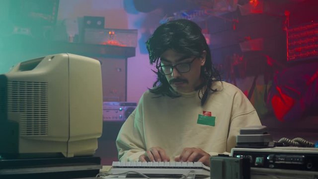 In the '80s or '90s young man using his personal computer typing on a keyboard. Retro scene with vintage colors and atmosphere.