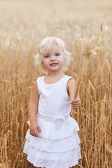 Portrait of handsome blond girl with blue eyes, face close up at summer time, in the wheat field. Cute little girl in the summer field of wheat. A child with a bouquet of wheat in his hands