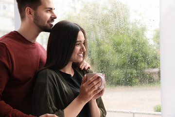 Happy young couple near window indoors on rainy day