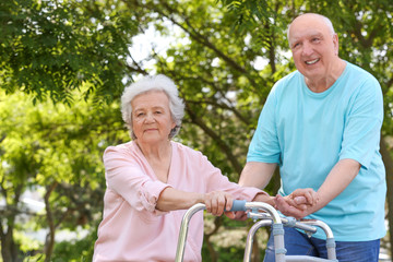 Elderly man helping his wife with walking frame outdoors