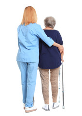 Caretaker helping elderly woman with walking frame on white background